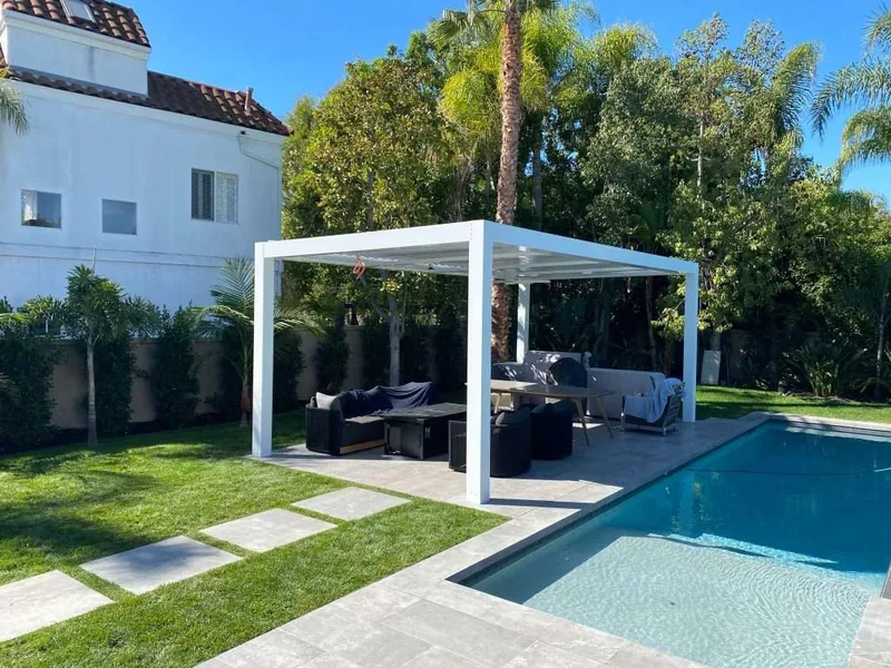 White freestanding Four Seasons louvered roof over a poolside lounge and dining area, blades open